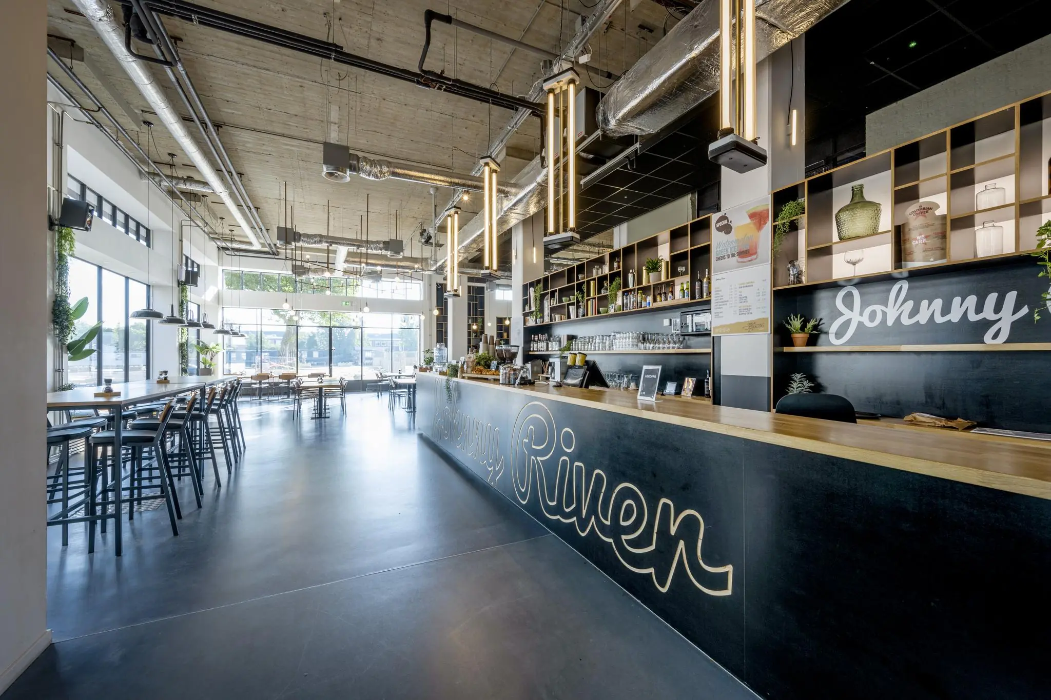 Moderne, ruim opgezette horecazaak aan de Joan Muyskenweg met industriële uitstraling en een lange bar met de naam "Johnny River".